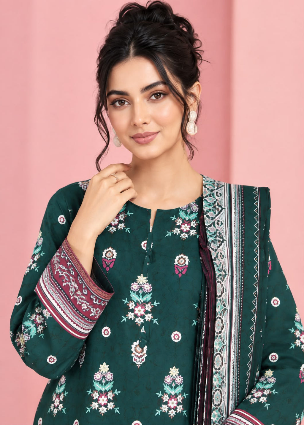A woman modeling a dark green unstitched salwar kameez suit with intricate multicolor floral embroidery and a matching patterned dupatta, set against a solid pink background.