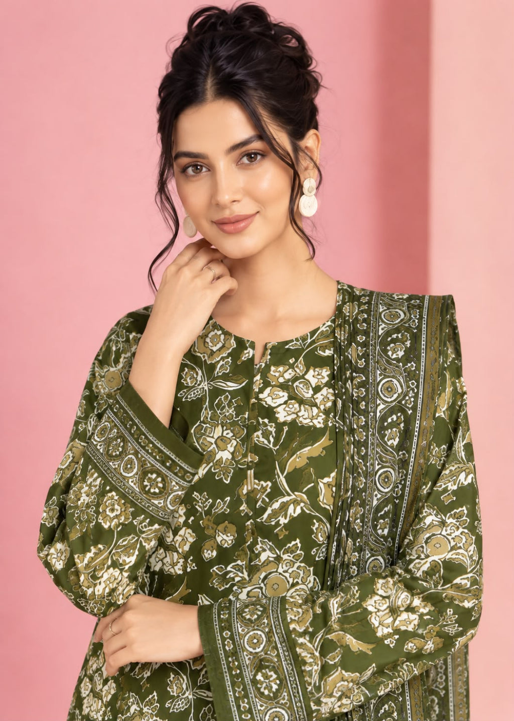 A woman wearing a green printed kurta with beige and white floral patterns, posed against a solid pink background.
