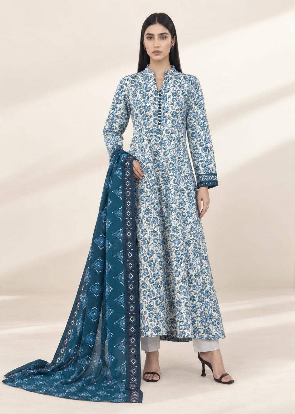 A woman models a traditional Indian outfit consisting of a long-sleeved blue and white floral printed kurta, paired with a matching blue printed dupatta, set against a warm beige studio background.