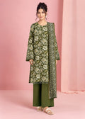 A woman models a three-piece olive green ethnic suit set featuring a long-sleeve kurta with white floral embroidery, matching wide-leg trousers, and a coordinating printed dupatta, set against a pink studio backdrop.