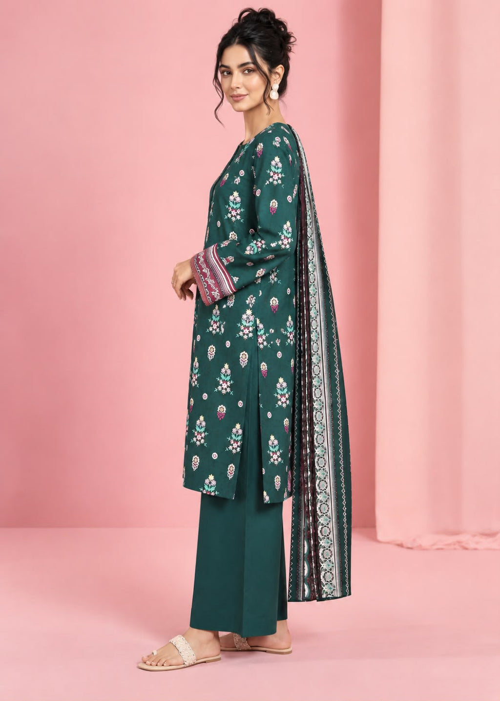 A woman models a dark green Indian ethnic salwar kameez suit with white and pink floral prints, paired with matching green trousers and a patterned dupatta, set against a solid pink backdrop.
