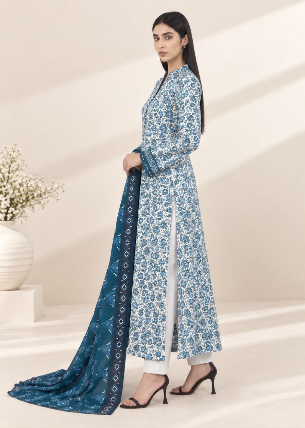 A woman models a traditional Indian salwar kameez suit set featuring a light blue and white floral print kurta with a matching dark blue printed dupatta, set against a warm beige background with soft shadows.