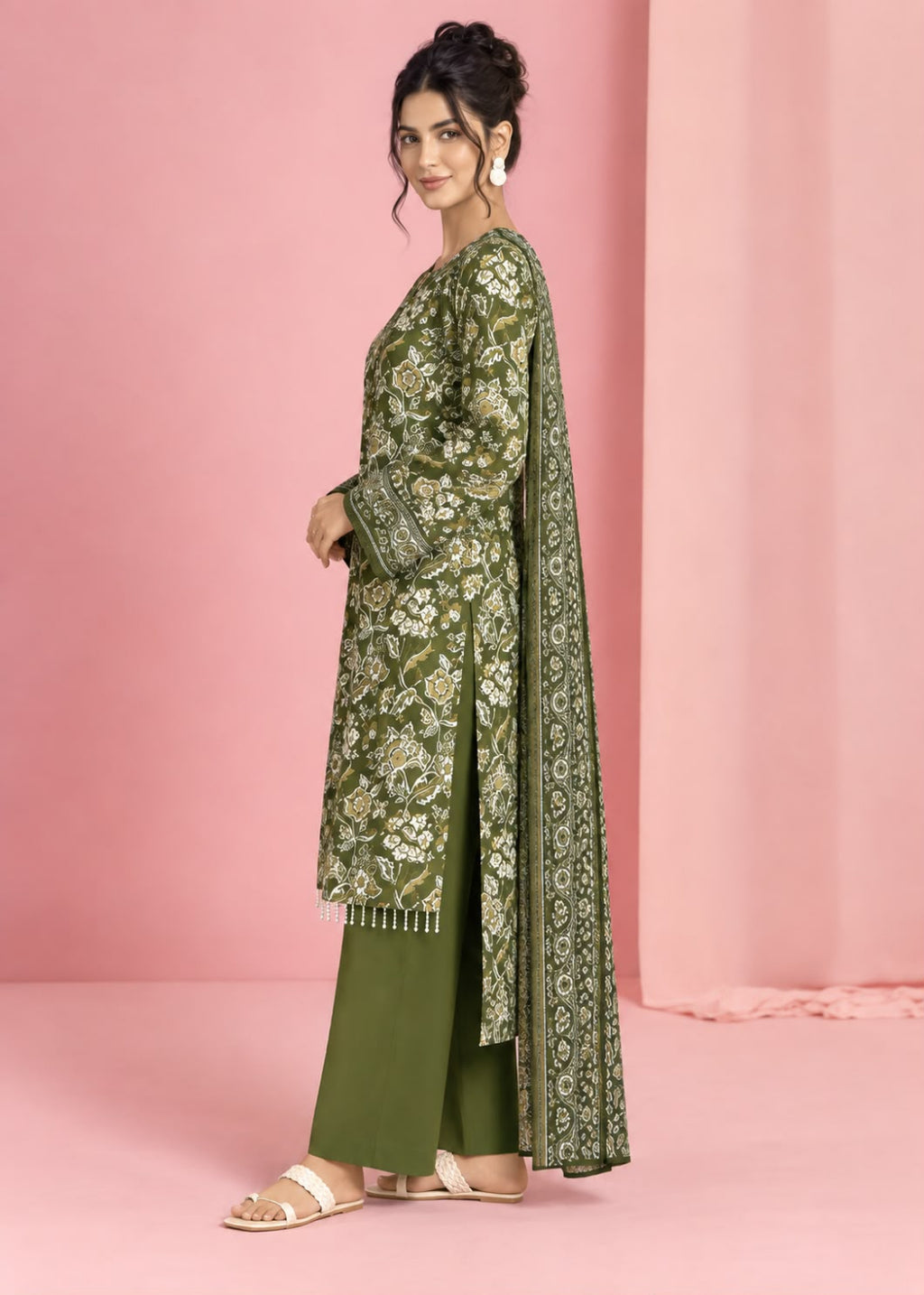 A woman models an olive green traditional outfit with intricate gold and white floral embroidery, paired with matching olive green pants, set against a solid pink studio backdrop.