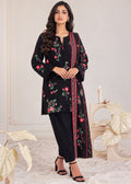 A woman models a black three-piece salwar kameez suit with floral embroidery and a red-trimmed dupatta, styled with black trousers and black high-heeled sandals in a neutral indoor setting.