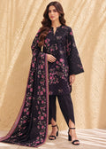 A woman modeling a black three-piece salwar kameez suit with pink and purple floral embroidery, paired with black pants and a matching dupatta, set against a textured beige backdrop.