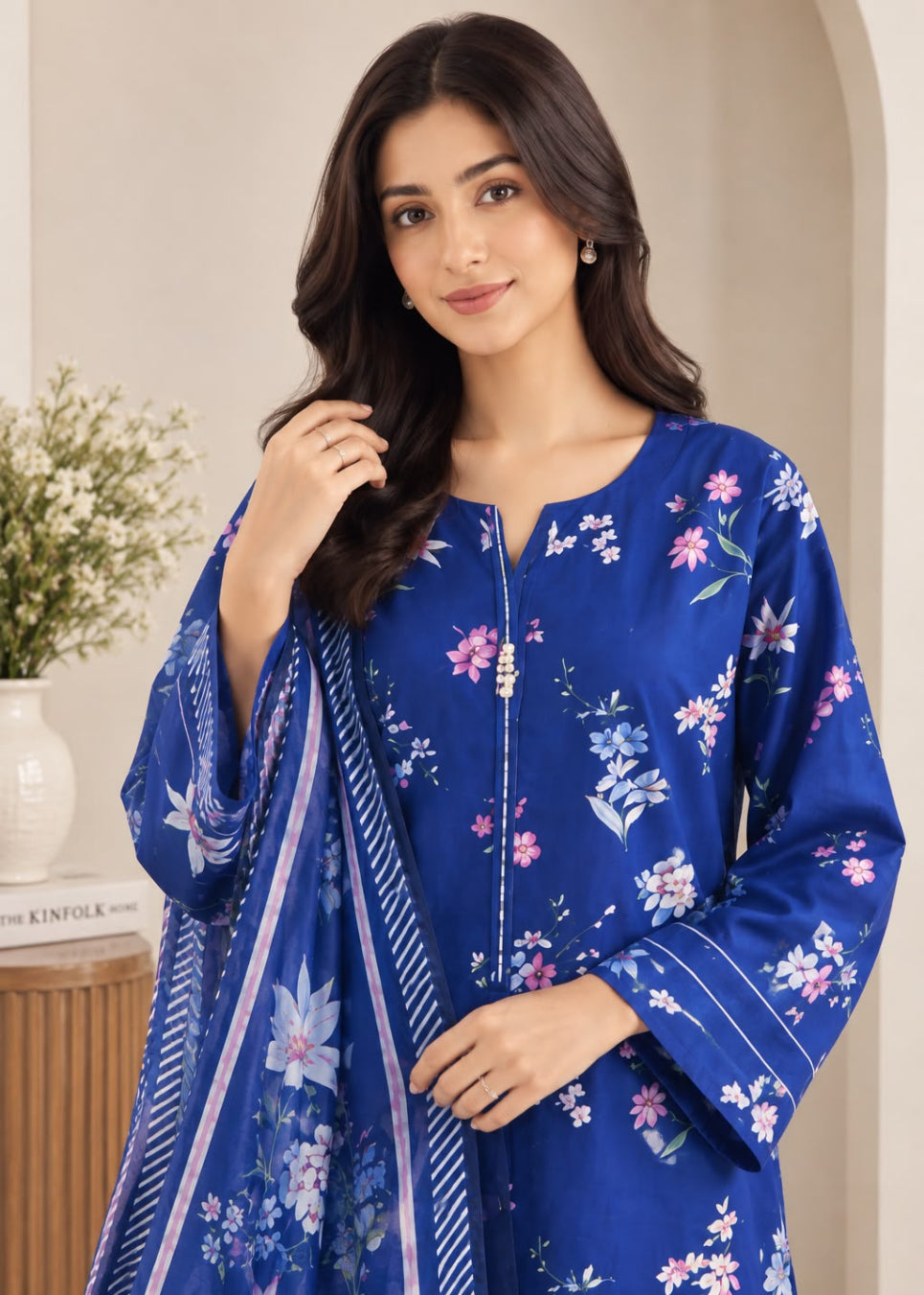 A woman wearing a royal blue floral printed kurta with a matching dupatta, standing in a softly lit indoor setting.