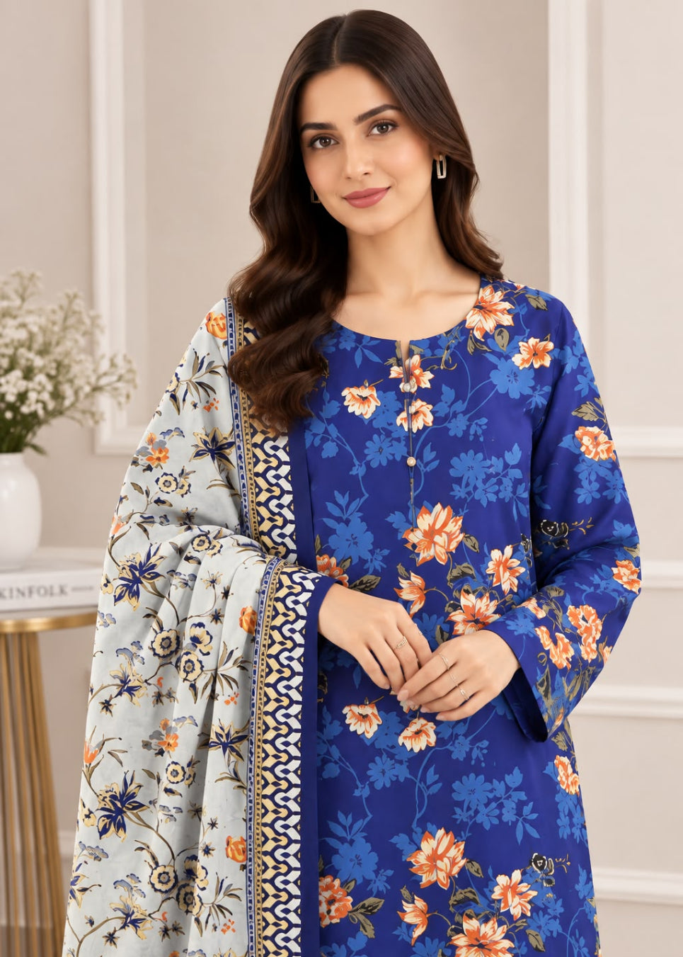 A woman modeling a royal blue floral salwar kameez suit with a matching dupatta. The suit features orange and yellow floral patterns, and the dupatta is light gray with blue and orange floral motifs and a black and gold border.