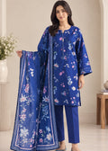 A woman models a royal blue three-piece salwar kameez suit with a floral print and a matching dupatta. The set includes a long-sleeved tunic, matching trousers, and a sheer dupatta with a white border and floral pattern, set against a warm beige background.