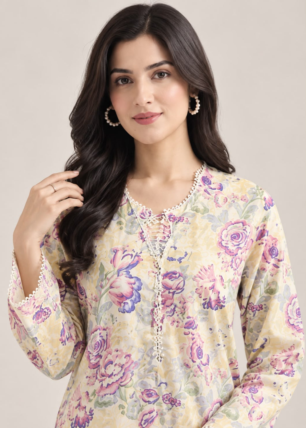 A woman modeling a cream-colored long-sleeve kurta with a purple and pink floral print, featuring a lace-up neckline with a beaded tassel.
