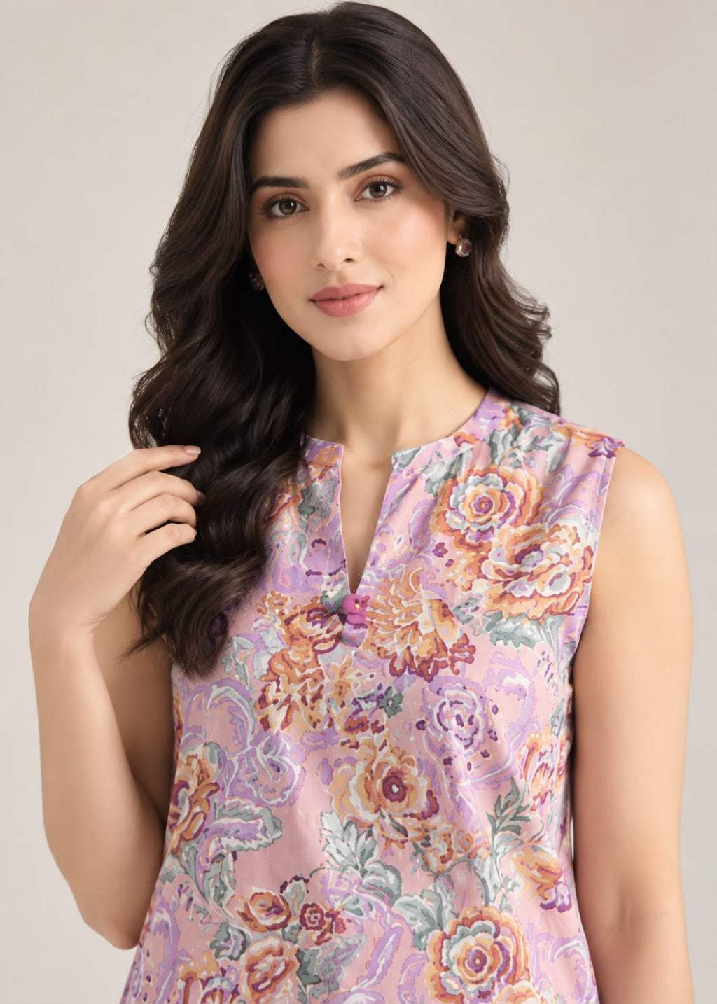 A woman wearing a sleeveless lavender floral top with a split neckline, photographed against a plain light beige studio background.