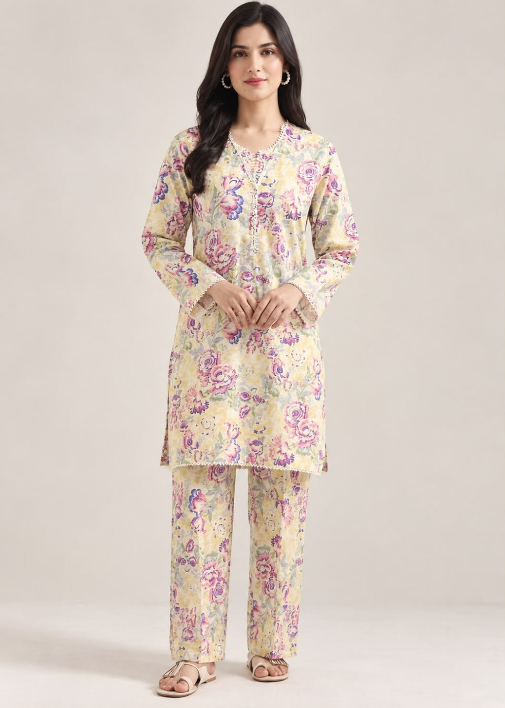 A woman modeling a two-piece Indian ethnic kurta set with matching trousers. The set features a light beige base with a vibrant floral print in purple, pink, and green.