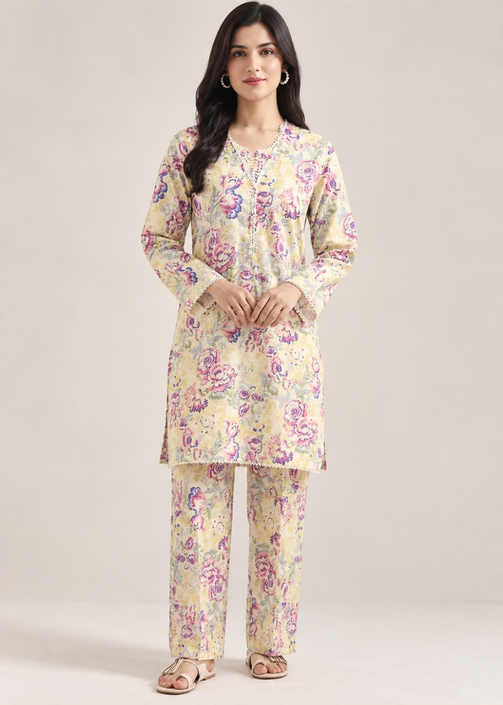 A woman modeling a two-piece Indian ethnic kurta set with matching trousers. The set features a light beige base with a vibrant floral print in purple, pink, and green.