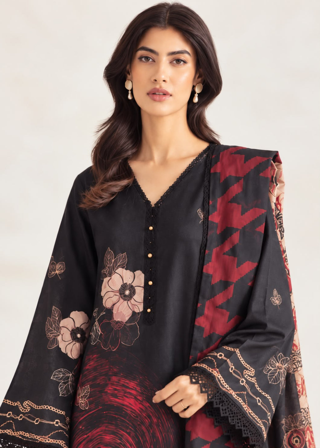 A woman modeling a black three-piece salwar kameez suit with floral prints and a red patterned dupatta, set against a plain light background.