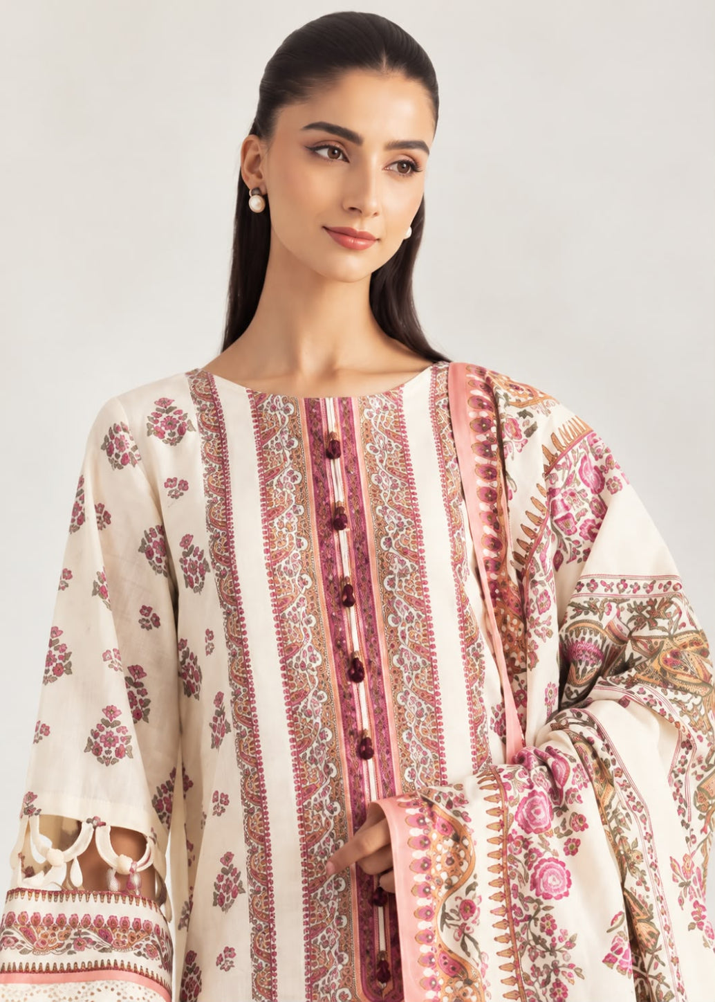 A woman wearing a cream-colored traditional embroidered tunic with pink and brown floral patterns and decorative buttons down the front, set against a plain light gray background.