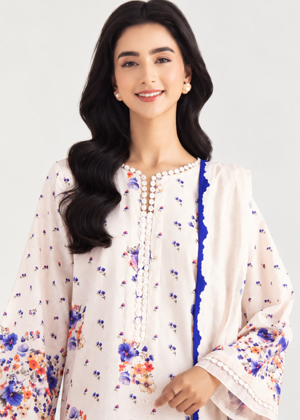 A woman modeling a white traditional kurta with blue and orange floral prints, featuring a blue and white scalloped border and a vertical line of white bead embellishments down the center front.