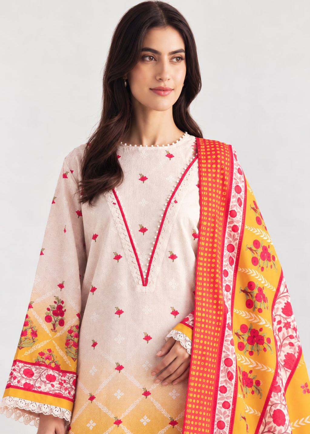 A woman modeling a traditional three-piece salwar kameez suit in light beige, featuring red embroidered details, a yellow and orange floral dupatta, and a red patterned border.