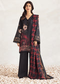 A woman models a black three-piece traditional outfit with red and gold floral patterns, featuring a long kurta, wide-leg trousers, and a matching dupatta, set against a neutral studio backdrop with decorative pebbles.