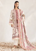 A woman models a traditional three-piece salwar kameez suit in cream with pink and brown floral prints, featuring a matching dupatta, set against a neutral studio backdrop with light-colored pebbles on the floor.
