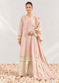 A woman models a traditional three-piece salwar kameez suit in light pink and beige. The kurta features vertical stripes, a V-neckline with a gold embroidered border, and lace-trimmed cuffs.