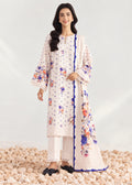 A woman models a traditional three-piece salwar kameez suit in off-white, featuring colorful floral embroidery in blue, orange, and purple, with a matching dupatta and white trousers, standing on a bed of light-colored pebbles.