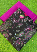 A folded black fabric piece with a colorful paisley and floral print, placed on bright green artificial grass with a folded magenta fabric piece behind it.