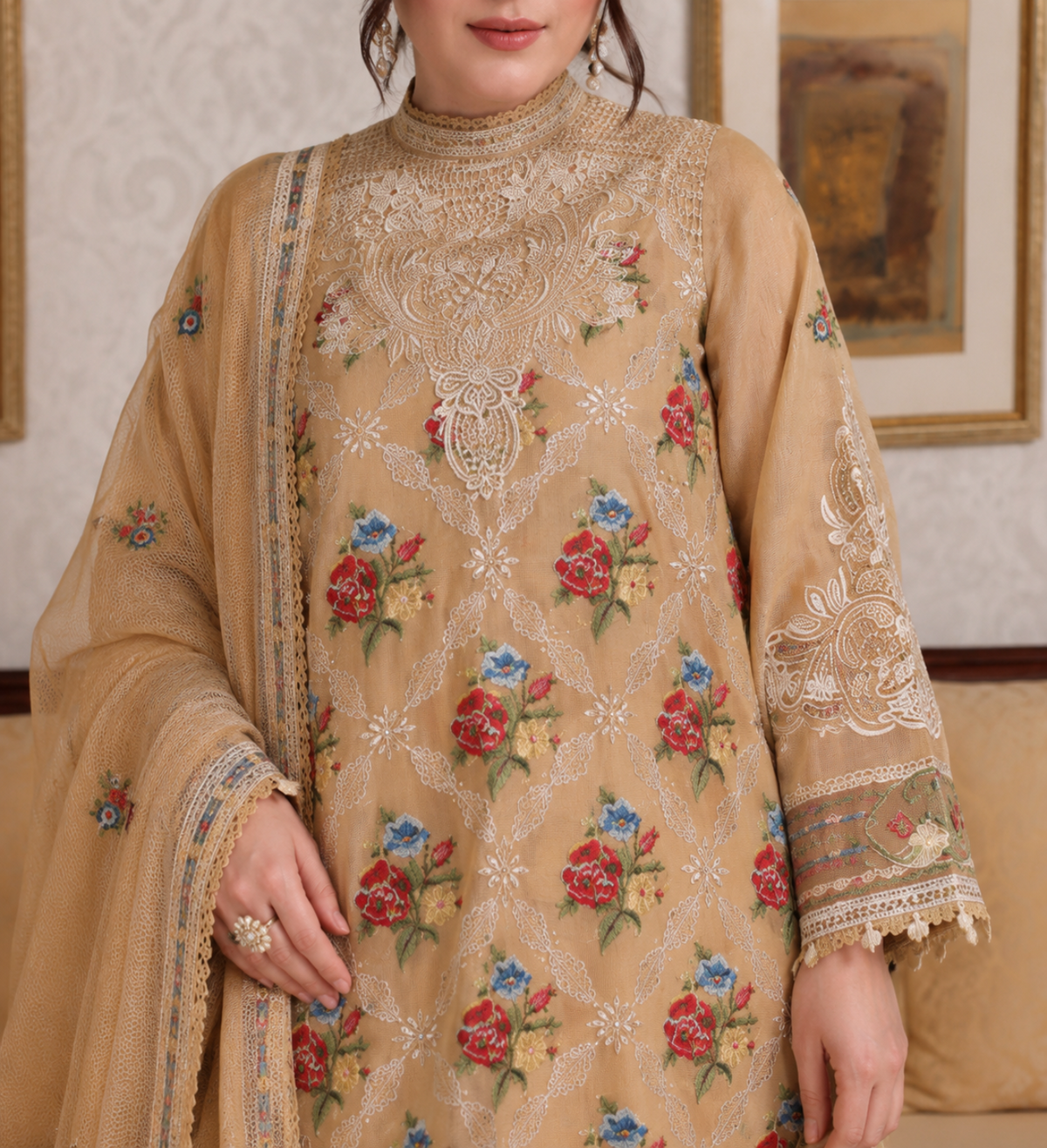 A woman wearing a beige embroidered traditional outfit with floral embroidery in red, blue, and green, paired with a matching dupatta. The image is cropped from the mouth down, showing detailed lace and mirror work on the chest and sleeves.