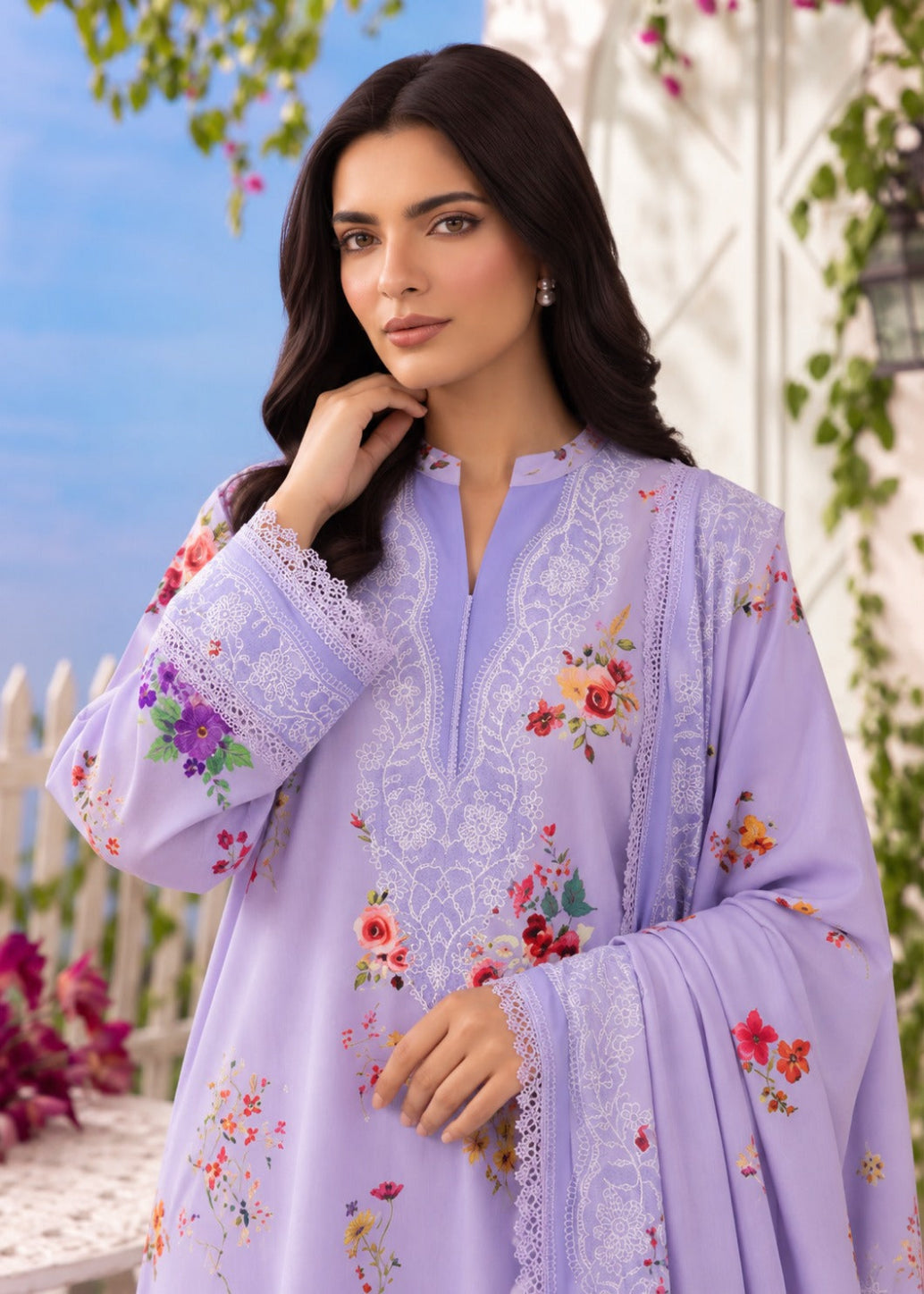 A woman wearing a lavender purple ethnic kurta with white floral embroidery and colorful floral prints, set against an outdoor garden background.