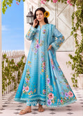 A woman models a long turquoise blue embroidered Anarkali gown with floral prints, set against a decorative outdoor background with a white door, green vines, and a blue sky.