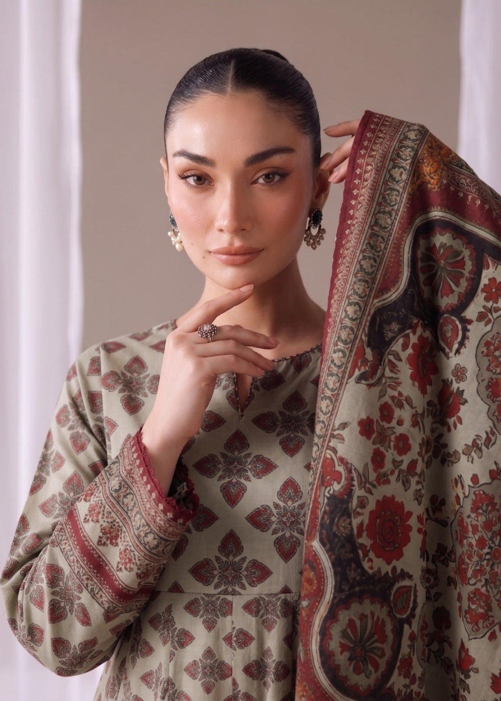 A woman models a traditional South Asian outfit featuring a beige kurta with red and brown floral patterns and a matching patterned dupatta draped over her shoulder.