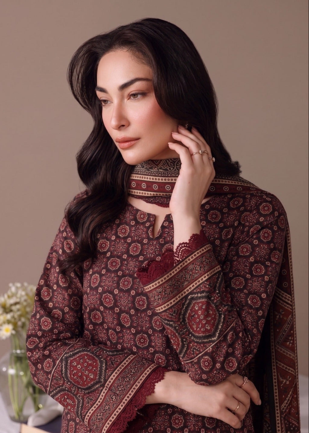 A woman wearing a dark brown and red patterned traditional outfit with lace trim, posed against a solid beige background.