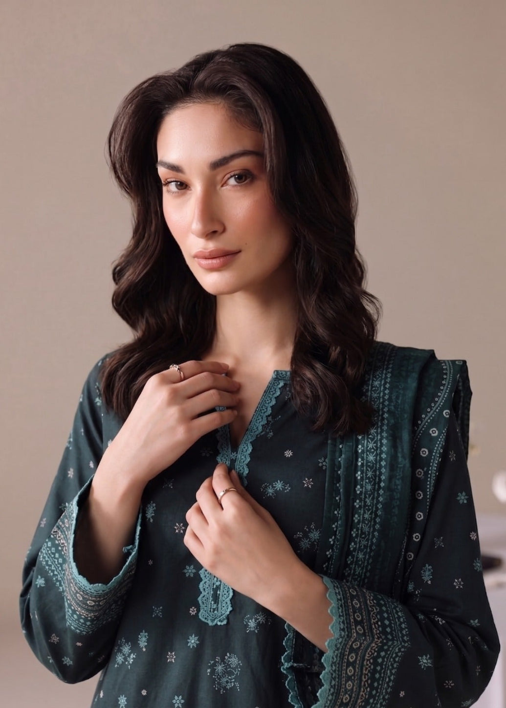 A woman wearing a dark teal green embroidered kurta with lace trim and delicate floral patterns, posing against a neutral beige background.