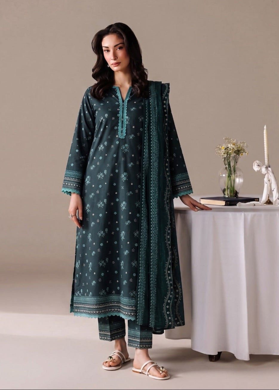 A woman models a dark teal green ethnic kurta set with white printed motifs and a matching dupatta, standing in a studio setting next to a white draped table.