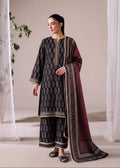 A woman models a traditional three-piece salwar kameez suit in a studio setting. The set features a dark gray printed kurta and matching trousers with gold borders, paired with a deep maroon dupatta that has gold and silver patterns.