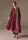 A woman modeling a traditional long kurta set in deep magenta with intricate floral prints, beige embroidery, and a matching printed dupatta, set against a solid warm beige studio background.