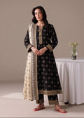 A woman models a black three-piece salwar kameez suit with beige and gold printed patterns, featuring a beige dupatta with a gold border, set against a neutral studio background with a white draped table.