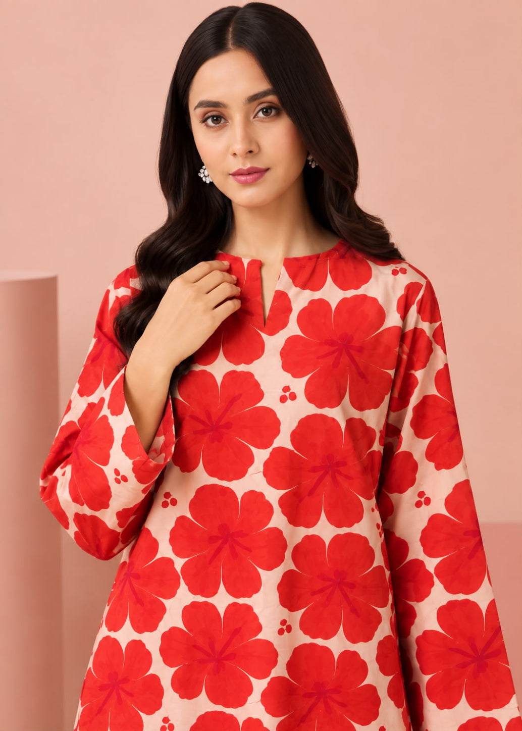 A woman wearing a long-sleeve cream-colored tunic top with a bold red floral pattern, posed against a solid pink studio background.