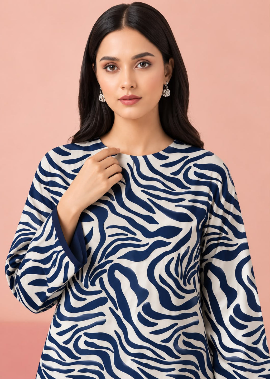 A woman modeling a long-sleeve top with a navy blue and white wavy zebra-like pattern against a solid pink background.