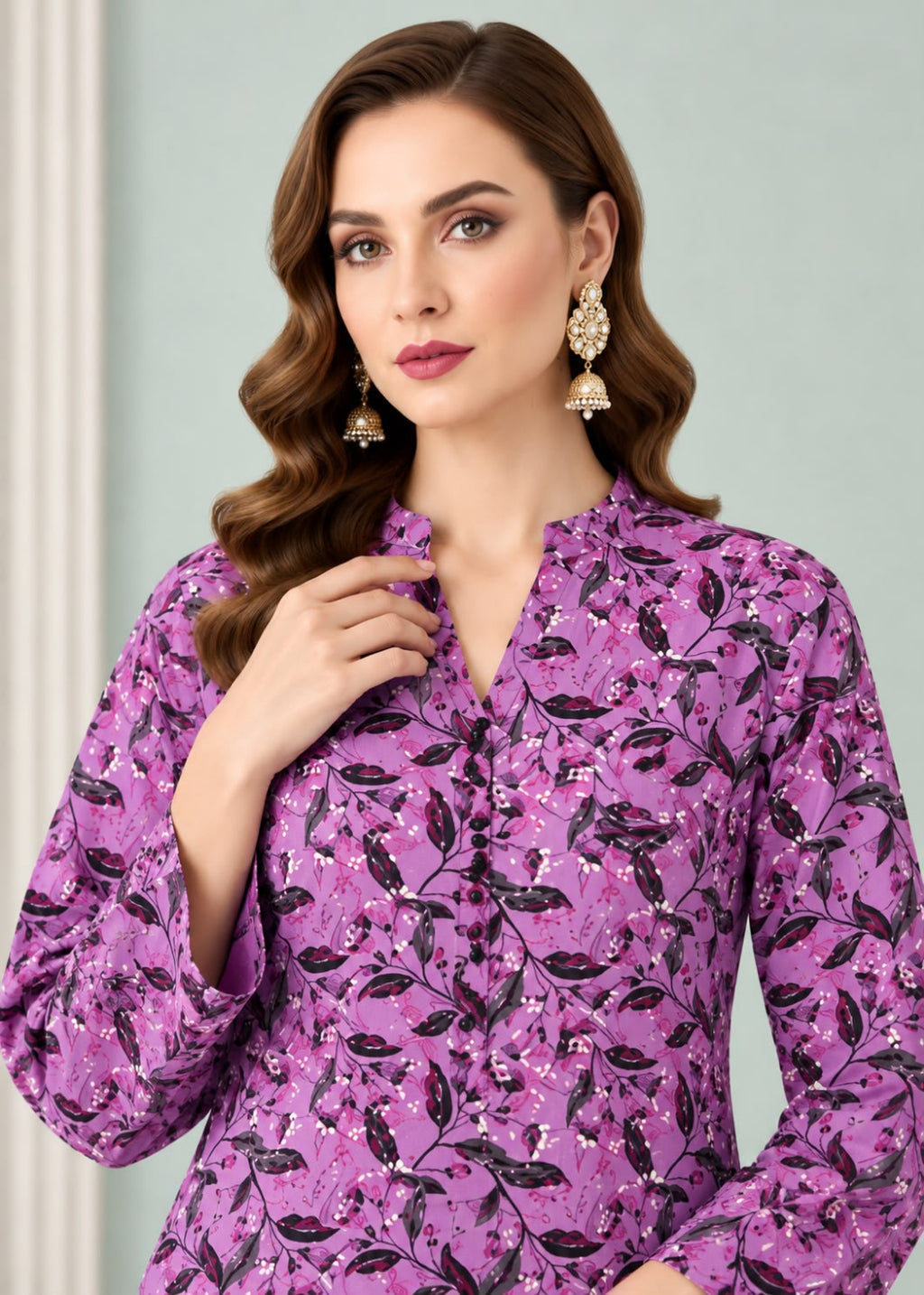 A woman wearing a purple long-sleeve blouse with a black and pink floral leaf pattern, styled with ornate gold earrings against a soft light gray background.