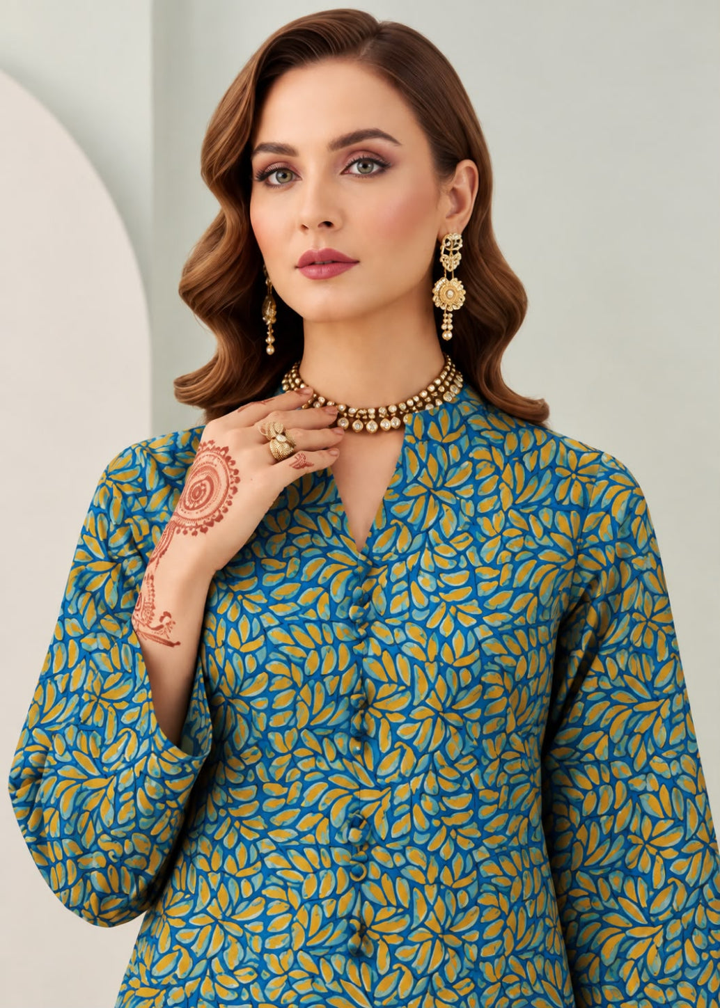 A woman modeling a teal blue and mustard yellow printed kurta with a high neckline, paired with gold jewelry against a light gray background.