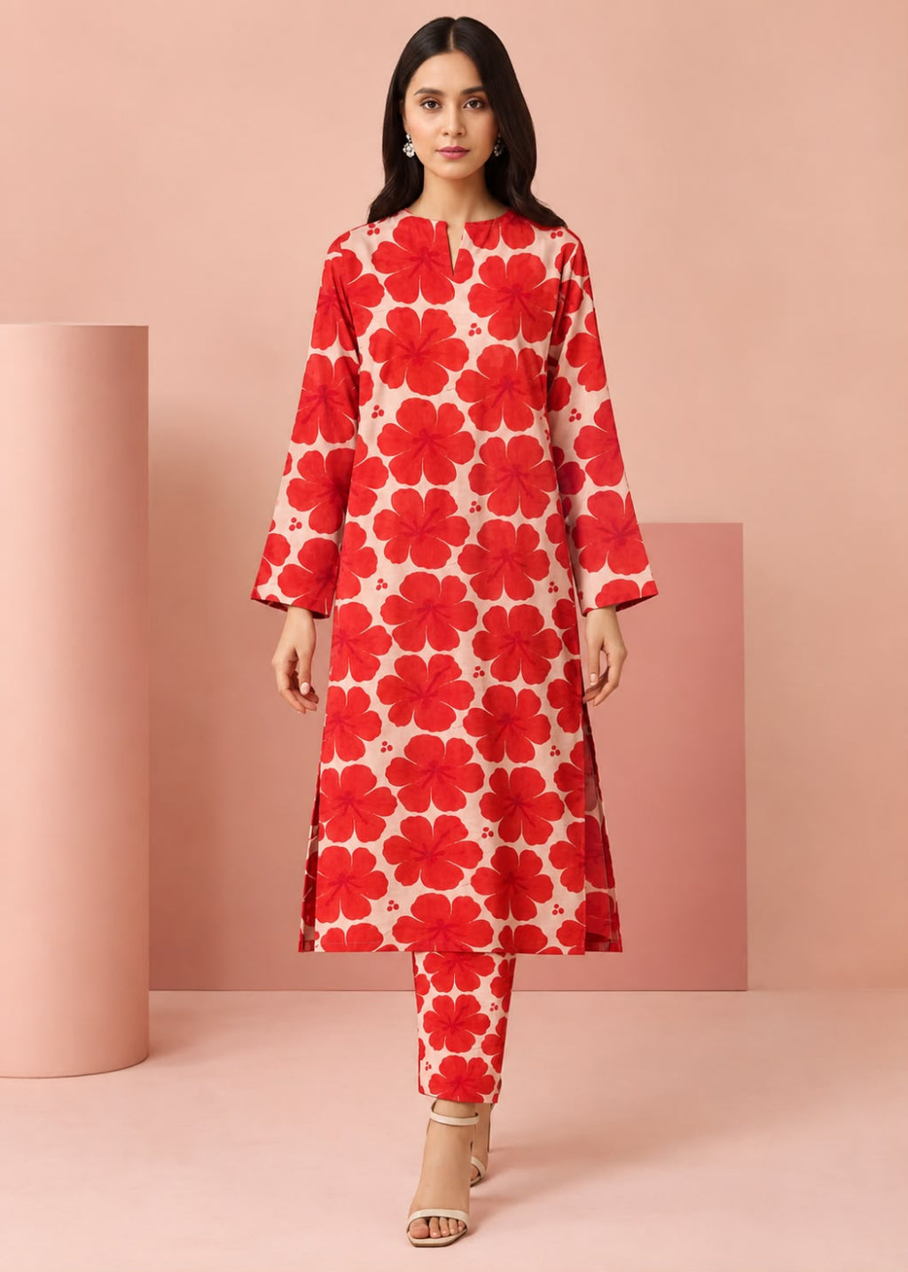 A woman modeling a red and cream floral print kurta set with matching pants, standing in a studio with pink geometric props.