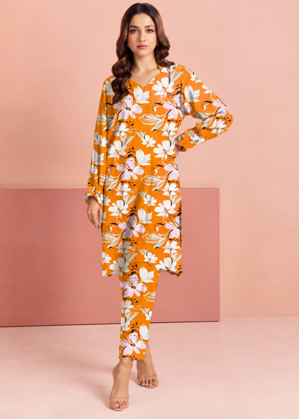 A woman modeling a matching orange floral long-sleeve tunic and trouser set against a pink studio backdrop.