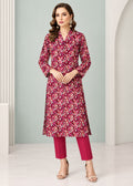 A woman models a long-sleeved floral kurta in deep magenta and burgundy with white accents, paired with matching magenta pants and beige high-heeled sandals, set against a light gray and white architectural background.