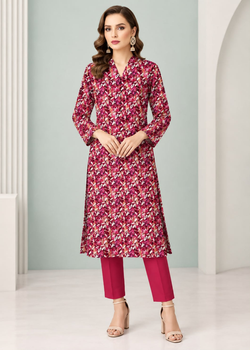 A woman models a long-sleeved floral kurta in deep magenta and burgundy with white accents, paired with matching magenta pants and beige high-heeled sandals, set against a light gray and white architectural background.