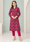 A woman modeling a long-sleeve floral printed kurta in magenta pink with black and white floral motifs, paired with matching pink pants and beige high-heeled sandals, set against a minimalist studio backdrop with white columns and arches.