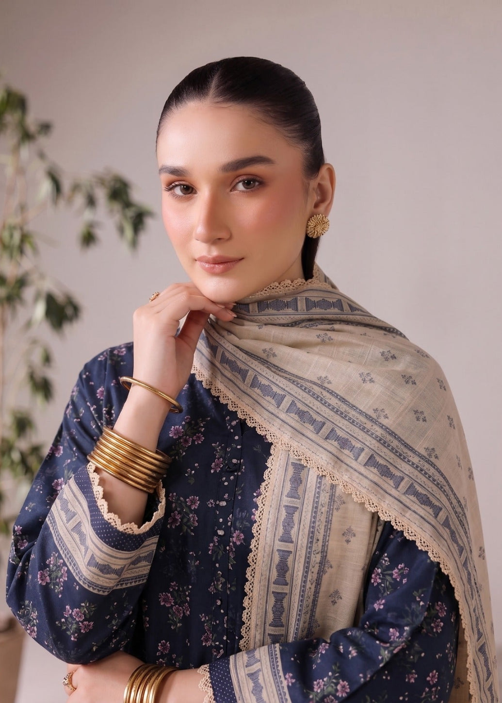 A woman modeling a navy blue floral printed kurta with a beige patterned dupatta featuring a scalloped border, styled with gold bangles and earrings against a neutral background.