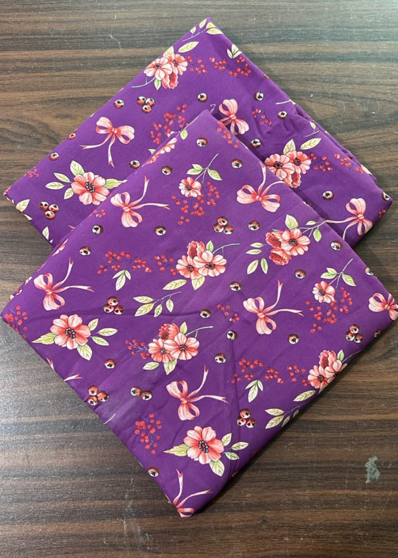 A folded purple quilt or comforter with a pink and white floral pattern, placed on a dark wood surface.