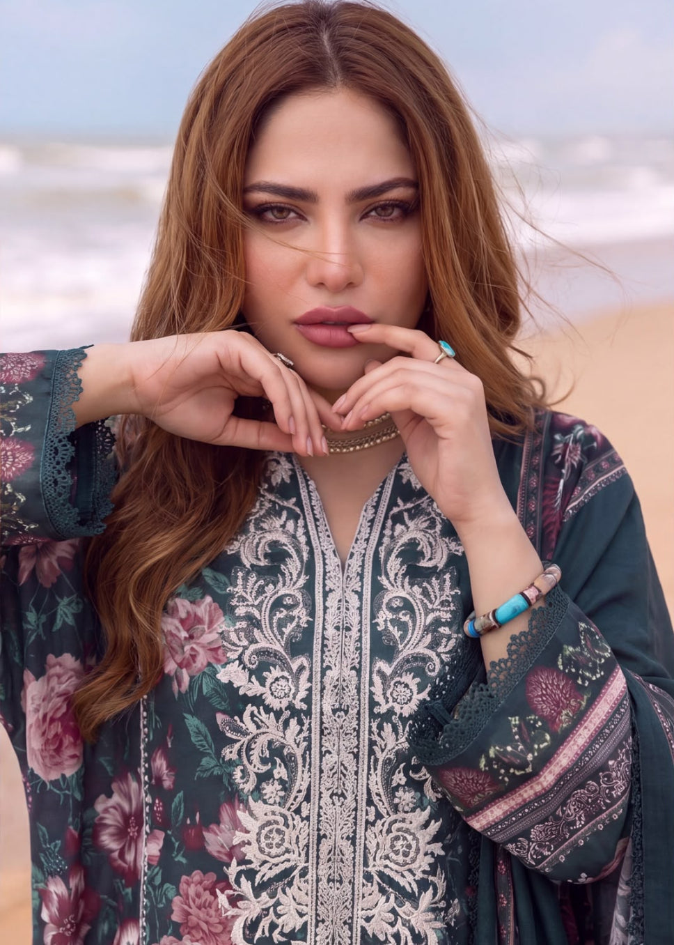 A woman posing on a beach wearing a dark teal green floral printed kurta with intricate white embroidery on the front panel.