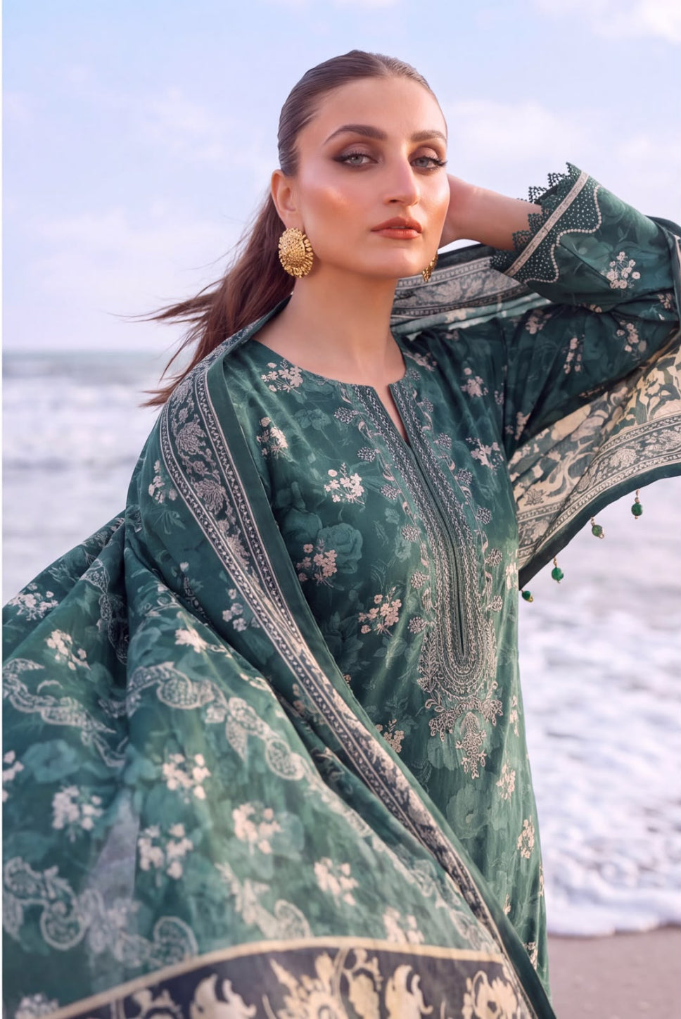 A woman posing on a beach wearing a dark green printed ethnic kurta with a matching dupatta and gold earrings.