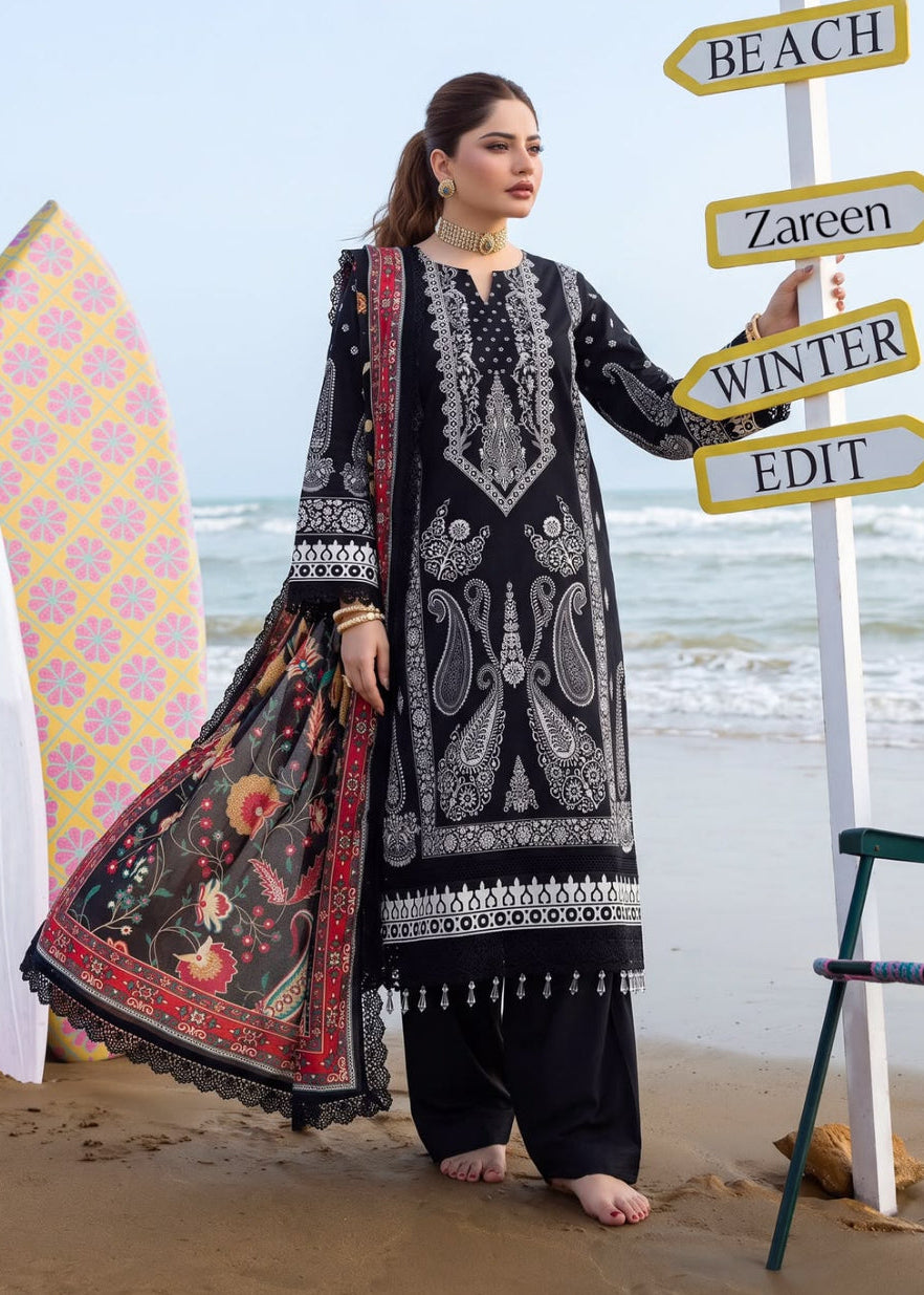 A woman stands on a sandy beach wearing a black and white embroidered traditional outfit with a red patterned dupatta. A large white directional signpost with words including SPA, BEACH, Zareen, WINTER, and EDIT is beside her, with surfboards and the ocean in the background.