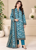 A woman models a traditional Indian salwar kameez suit set in a styled indoor setting. The set features a teal blue printed kurta with white and yellow floral motifs and gold borders, paired with matching teal pants and a coordinating dupatta.